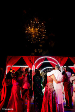 A group of people in festive attire watch fireworks above a red-decorated outdoor venue at night.