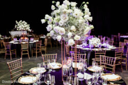 Elegant banquet table setup with gold chairs, purple tablecloths, and a tall white floral centerpiece.