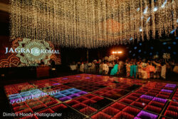 A decorated wedding reception hall with hanging string lights, LED dance floor, and guests seated at round tables.