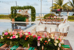 Outdoor beachside event setup with floral arrangements, wicker furniture, and a green velvet sofa near the ocean.
