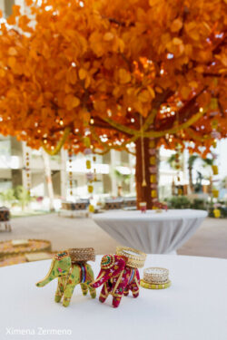 Two decorative elephants and gold bangles on a table with an orange artificial tree in the background.