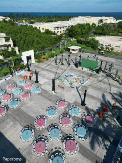 Aerial view of an outdoor event setup with round tables, decorated chairs, and a colorful dance floor.