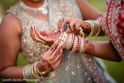 A close-up of two women in traditional attire adjusting bangles, with intricate henna designs visible on their hands.