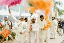 A group of men in traditional attire celebrate outdoors with orange and red smoke bombs at a festive event.